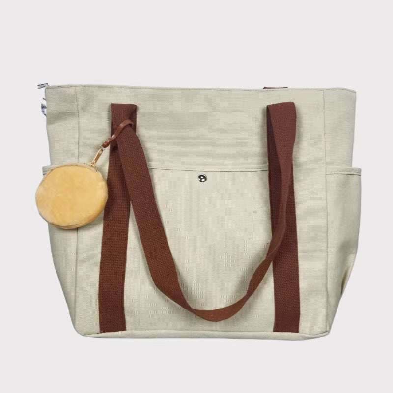 Large canvas shoulder bag with brown straps and a round pouch attachment, ideal for work and commuting.