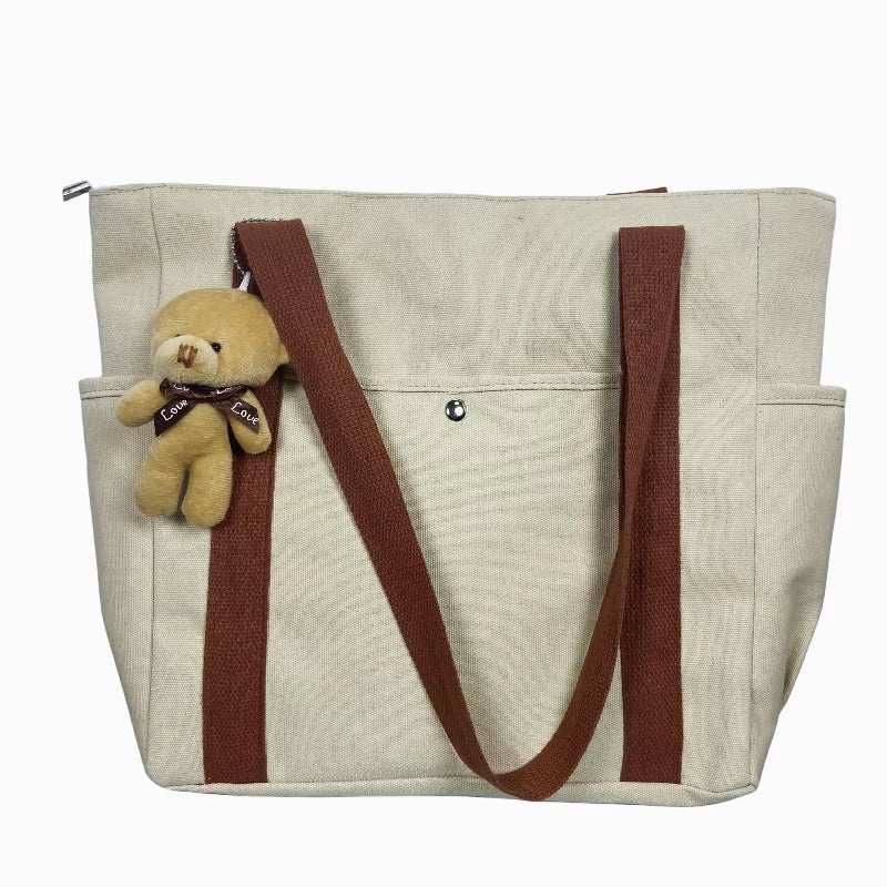 Large canvas shoulder bag with brown straps and teddy bear keychain, ideal for work and commuting.