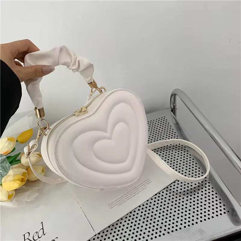 Heart shape white shoulder bag in PU leather with top handle on a table.
