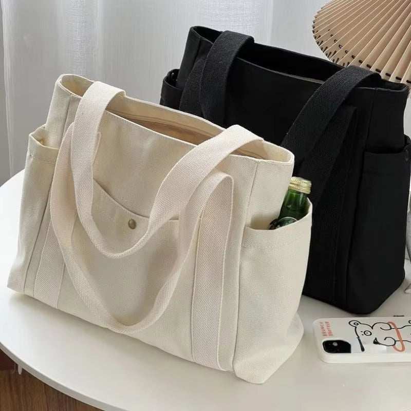 Large canvas shoulder bags in white and black on a table, ideal for work and commuting.