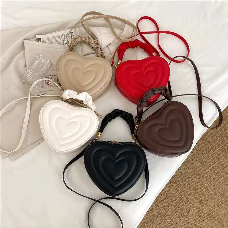 Heart-shaped PU leather shoulder bags in various colors, including black, red, white, coffee, and khaki.