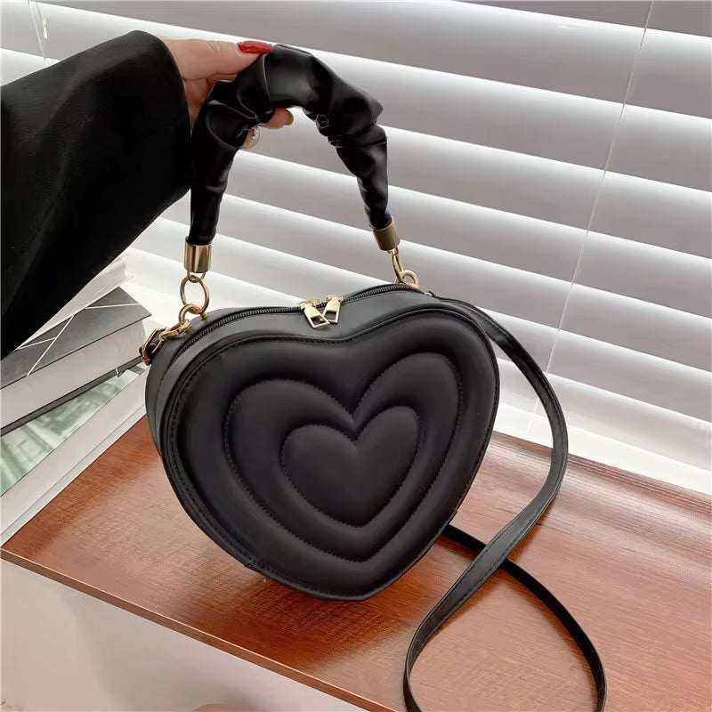 Heart-shaped black PU leather shoulder bag with top handle and crossbody strap.